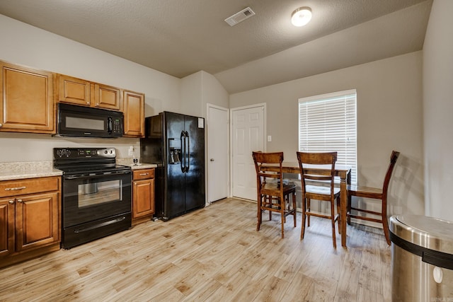 kitchen with visible vents, lofted ceiling, light countertops, light wood finished floors, and black appliances