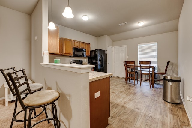 kitchen with brown cabinetry, visible vents, a breakfast bar area, light countertops, and black appliances