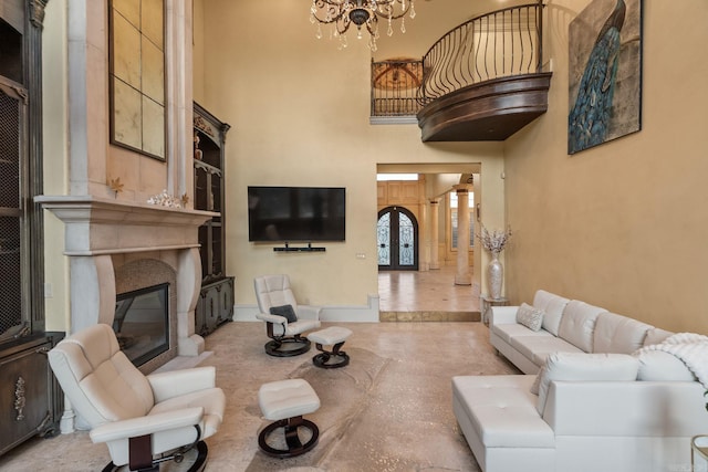 living area featuring french doors, a glass covered fireplace, a high ceiling, and a chandelier