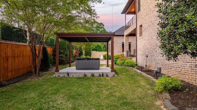 yard at dusk with a patio, a fenced backyard, and a hot tub