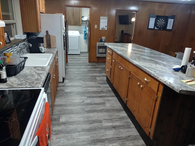 kitchen with electric range, washer / clothes dryer, brown cabinets, wood finished floors, and light countertops