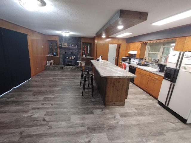 kitchen with a sink, white refrigerator with ice dispenser, light countertops, stainless steel microwave, and under cabinet range hood