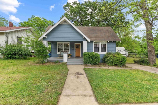 bungalow-style home with roof with shingles, covered porch, and a front lawn