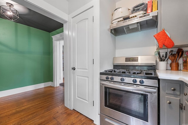 kitchen with ventilation hood, stainless steel gas stove, light countertops, gray cabinetry, and dark wood-style floors