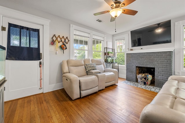 living area with a ceiling fan, visible vents, a brick fireplace, hardwood / wood-style flooring, and baseboards