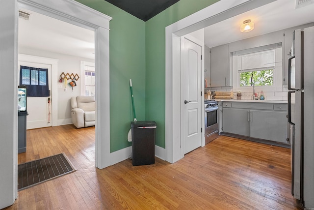 kitchen featuring stainless steel gas range, a sink, visible vents, light wood-style floors, and gray cabinetry