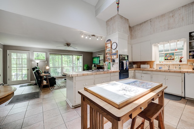 kitchen featuring white cabinets, a sink, a peninsula, tile countertops, and light tile patterned floors