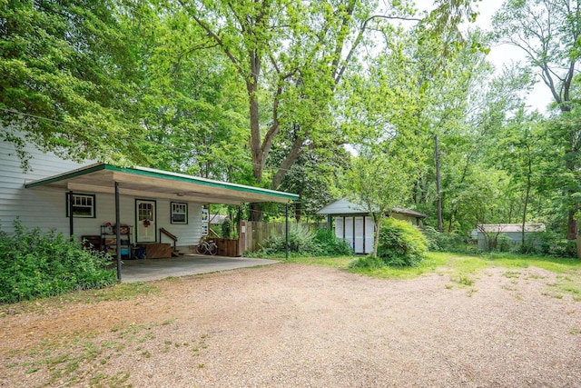 view of front of home featuring dirt driveway, fence, an outbuilding, and an attached carport