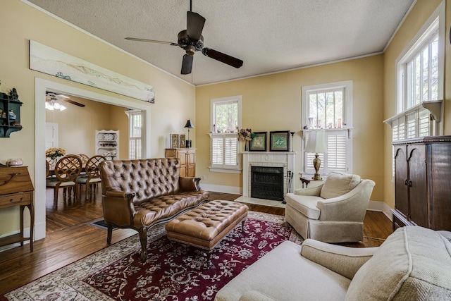 living room featuring ceiling fan, a textured ceiling, a tiled fireplace, wood finished floors, and ornamental molding