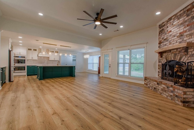 unfurnished living room with crown molding, ceiling fan, a fireplace, and light wood finished floors