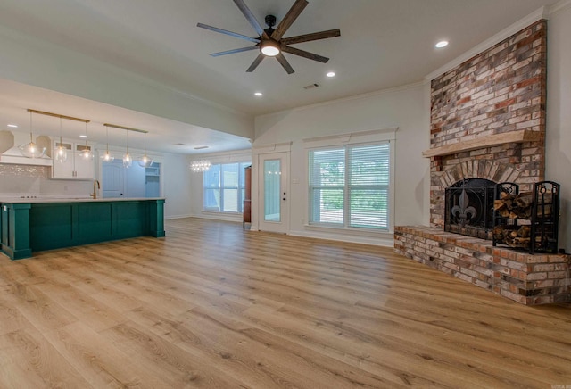unfurnished living room featuring light wood-style floors, ornamental molding, a fireplace, and ceiling fan