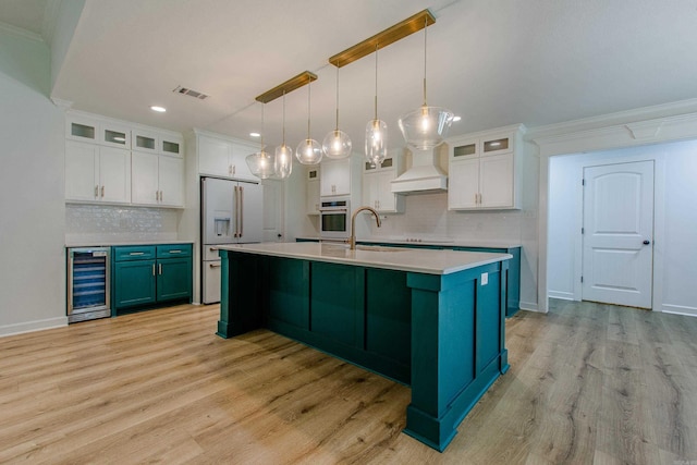 kitchen featuring visible vents, wall oven, high end white refrigerator, beverage cooler, and white cabinetry