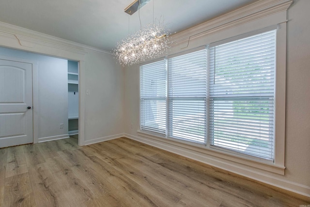 unfurnished dining area with crown molding, a notable chandelier, plenty of natural light, baseboards, and wood finished floors