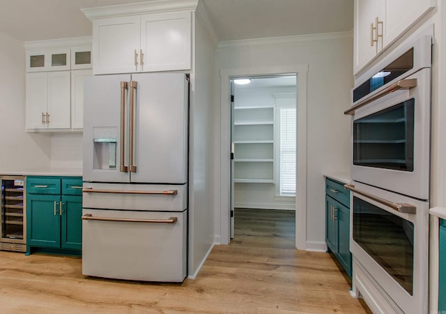 kitchen featuring white cabinetry, beverage cooler, ornamental molding, white appliances, and light wood-style flooring