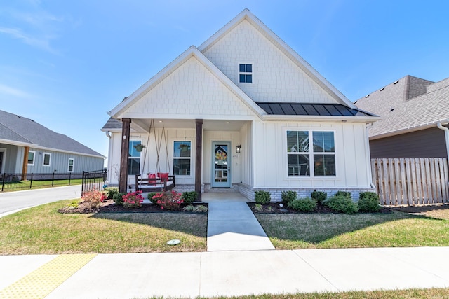 modern inspired farmhouse featuring a porch, board and batten siding, a standing seam roof, a front yard, and fence