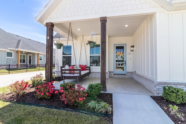 view of exterior entry featuring board and batten siding, fence, and covered porch