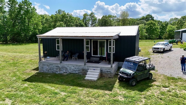 rear view of house with board and batten siding, a lawn, and covered porch