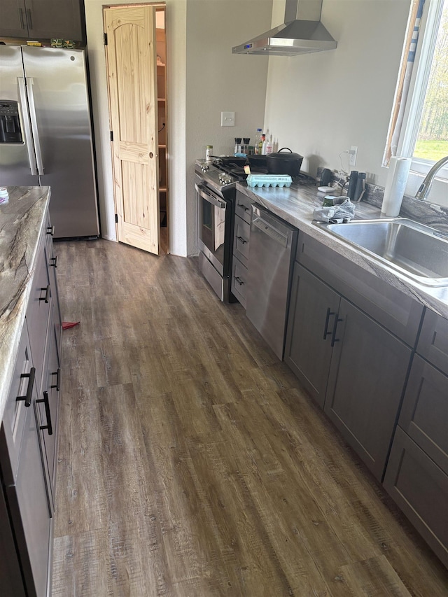 kitchen featuring wall chimney range hood, appliances with stainless steel finishes, gray cabinetry, a sink, and dark wood-style floors