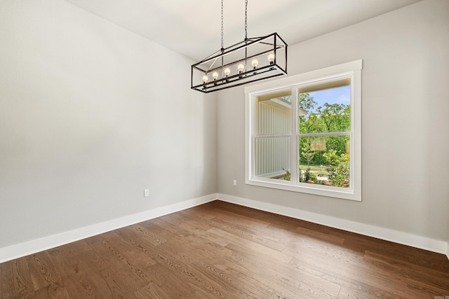 unfurnished dining area featuring an inviting chandelier, baseboards, and dark wood-style flooring