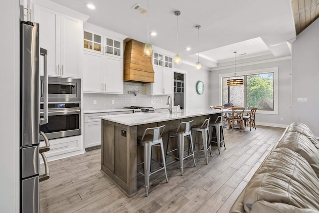 kitchen featuring visible vents, premium range hood, light wood-type flooring, a tray ceiling, and appliances with stainless steel finishes