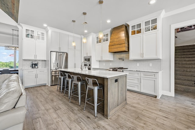 kitchen with appliances with stainless steel finishes, light wood-style floors, a kitchen breakfast bar, premium range hood, and open floor plan