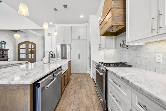 kitchen featuring white cabinets, appliances with stainless steel finishes, a sink, and premium range hood