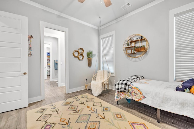bedroom featuring ceiling fan, visible vents, crown molding, wood finished floors, and baseboards