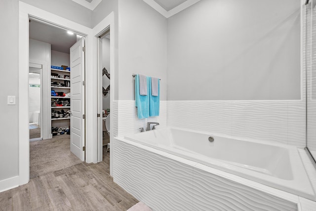 bathroom featuring ornamental molding, a walk in closet, a garden tub, and wood finished floors