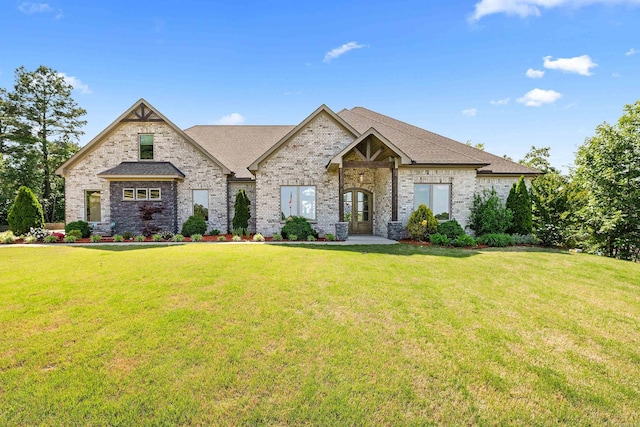 french country home with brick siding, a shingled roof, a front lawn, and french doors