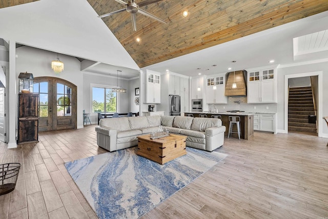 living area featuring ceiling fan, french doors, stairway, high vaulted ceiling, and light wood-style floors