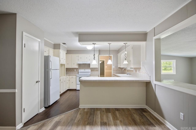 kitchen featuring white appliances, tile countertops, a peninsula, under cabinet range hood, and dark wood-style floors