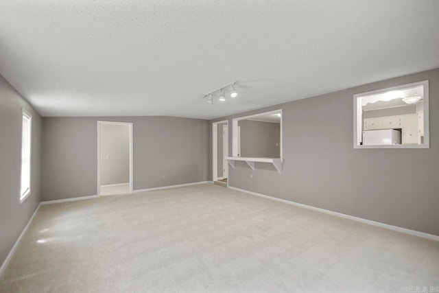 below grade area with carpet flooring, fridge, baseboards, and rail lighting