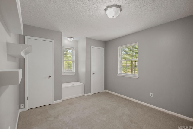 unfurnished bedroom featuring baseboards, light carpet, two closets, and a textured ceiling