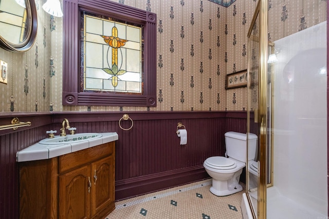bathroom with toilet, wallpapered walls, wainscoting, and a stall shower
