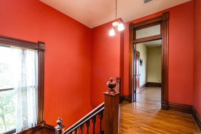 corridor with a healthy amount of sunlight, baseboards, wood finished floors, and an upstairs landing