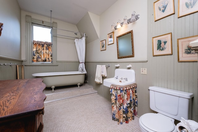bathroom with wainscoting, toilet, and a soaking tub