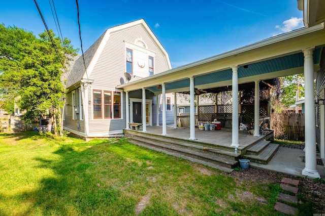 rear view of property with a lawn, fence, a deck, and a gambrel roof