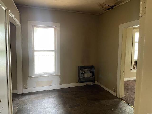 empty room with heating unit, baseboards, crown molding, and a wood stove