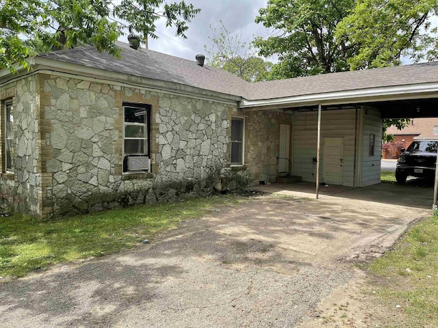 ranch-style house featuring roof with shingles, cooling unit, aphalt driveway, stone siding, and an attached carport