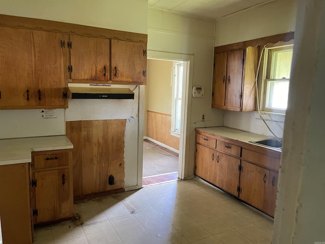 kitchen featuring under cabinet range hood, brown cabinets, and light countertops