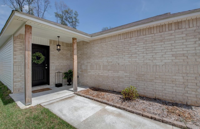 view of exterior entry with a porch and brick siding