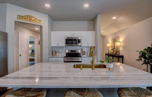 kitchen featuring light stone counters, a sink, a breakfast bar area, stainless steel appliances, and backsplash