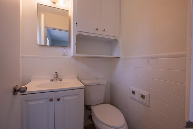 half bath featuring wainscoting, tile walls, vanity, and toilet