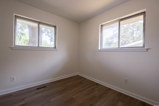 empty room featuring visible vents, dark wood-style flooring, baseboards, and a wealth of natural light