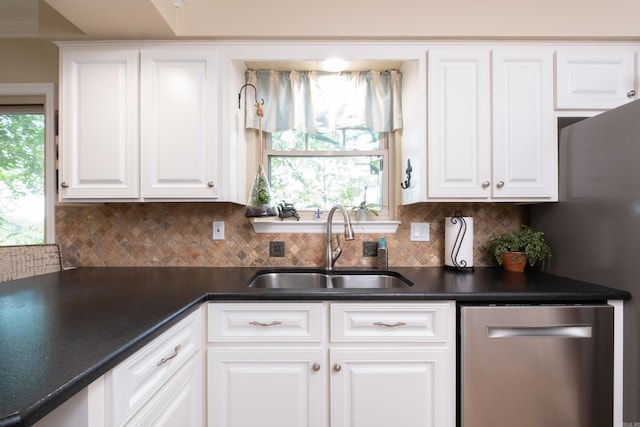 kitchen with dark countertops, tasteful backsplash, stainless steel dishwasher, a sink, and white cabinets