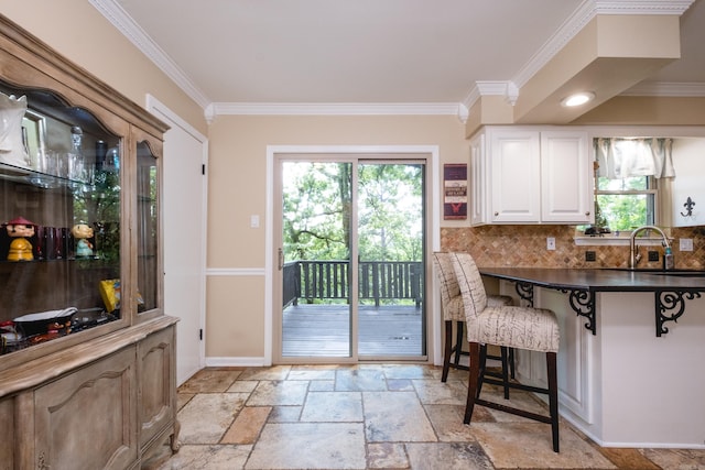kitchen featuring white cabinets, a sink, a kitchen breakfast bar, tasteful backsplash, and ornamental molding