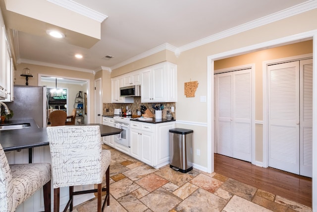 kitchen featuring crown molding, stone tile floors, dark countertops, white cabinets, and stainless steel appliances