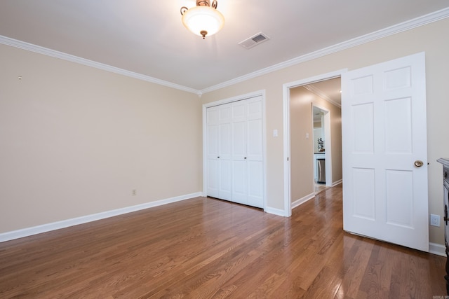 unfurnished bedroom with visible vents, crown molding, wood finished floors, baseboards, and a closet