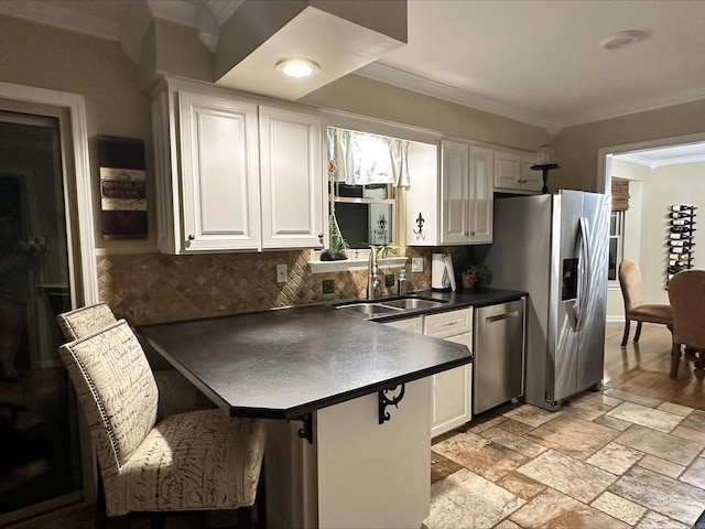 kitchen featuring crown molding, white cabinets, appliances with stainless steel finishes, a sink, and backsplash