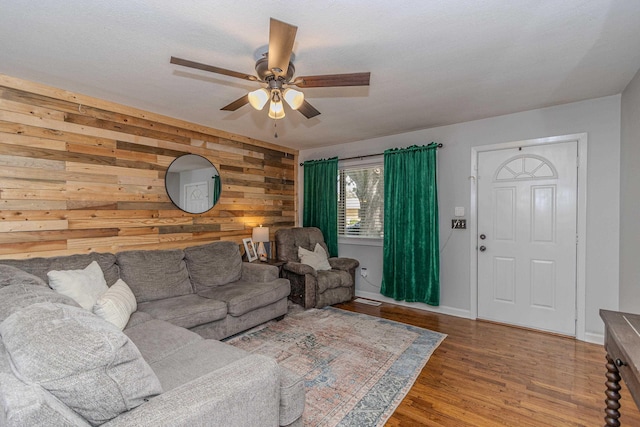 living room with wooden walls, a ceiling fan, baseboards, and wood finished floors